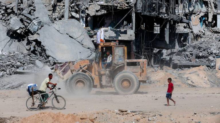 Rakyat Palestin melintasi runtuhan, ketika gencatan senjata antara Israel dan Hamas di Gaza, di Khan Younis, selatan Semenanjung Gaza, pada 14 Oktober 2025 - Reuters