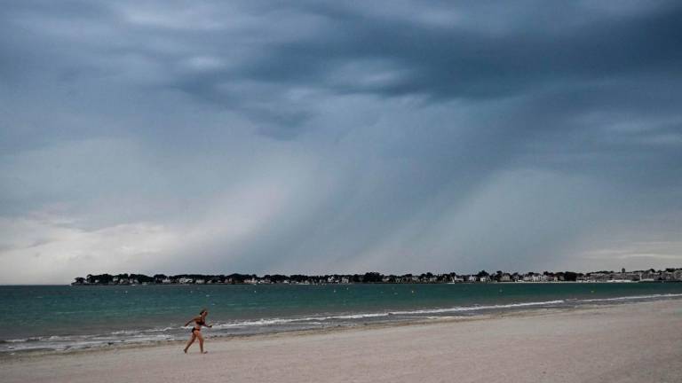 A woman walks on the beach as heavy rain falls during a thunder storm over the city of La Baule, western France, on June 25, 2025. (Photo by Loic VENANCE / AFP)