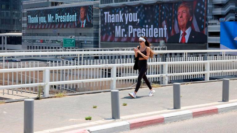 A woman walks on a bridge in front of banners bearing a pictures of US President Donald Trump accompanied by a messages, in Tel Aviv on June 22, 2025. (Photo by AHMAD GHARABLI / AFP)