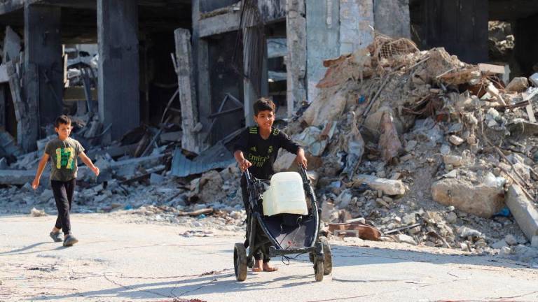Displaced Palestinian children walk, as one of them moves a cart loaded with water containers, amid a ceasefire between Israel and Hamas, in Gaza City, October 19, 2025. REUTERS/Ebrahim Hajjaj