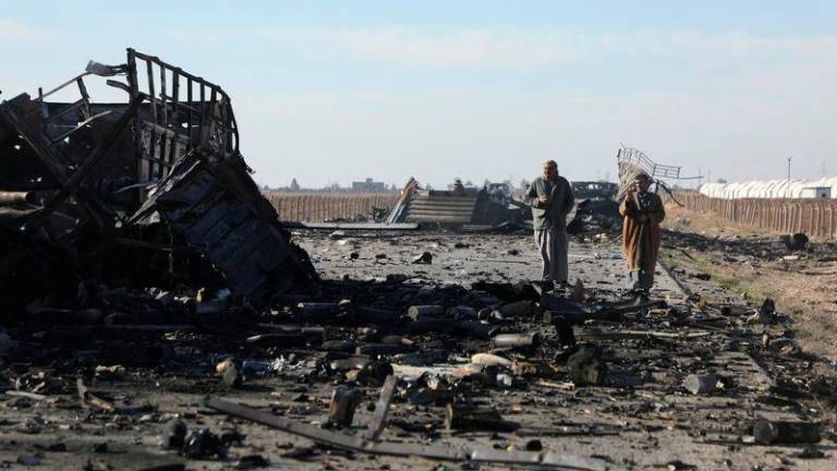 People walk by a burnt-out truck near Qamishli International Airport, after regional security sources and officers within the now-fallen Syrian army said that Israeli airstrikes continued against military installations and airbases overnight across Syria, December 10, 2024. REUTERS/Orhan Qereman