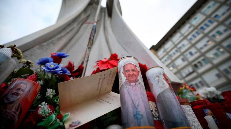 A candle with an image of Pope Francis and a card lie near the statue of the late Pope John Paul II outside the Gemelli Hospital, where Pope Francis is admitted to continue treatment for his ongoing respiratory tract infection, in Rome - REUTERSpix