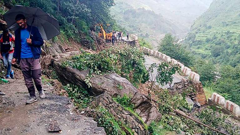 People stand beside a damaged road at a village near Uttarkashi on August 6, 2025, a day after a cloudburst caused a massive mudslide and flash floods in India’s Uttarakhand state. (Photo by AFP)