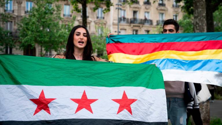 A woman holding the flag of Syria takes part in a demonstration at Place de la République organised by Kurd, Alawite and Druze minority groups of Syria, protesting the visit of Syria’s interim President,in Paris on May 7, 2025. (Photo by LEO VIGNAL / AFP)