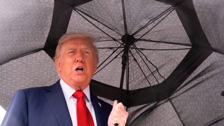 US President Donald Trump holds an umbrella as he speaks to reporters before boarding Air Force One prior to departure from Joint Base Andrews in Maryland, October 12, 2025. - AFP