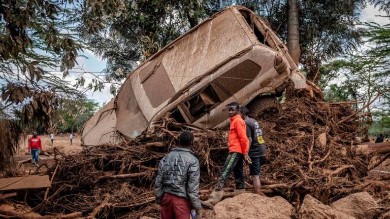 Young men inspect a destroyed car carried by waters in an area heavily affected by torrential rains and flash floods in the village of Kamuchiri, near Mai Mahiu, on April 29, 2024. At least 45 people died when a dam burst its banks near a town in Kenya’s Rift Valley, police said on April 29, 2024, as torrential rains and floods battered the country/AFFPix
