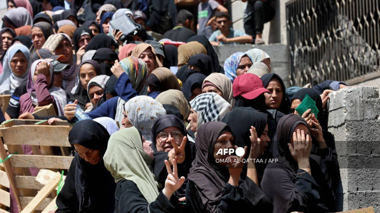Palestinian women flash the V for victory sign as they line up to receive bags of flour at a UN World Food Programme (WFP) warehouse on Al-Jalaa street in Gaza City, in the central Gaza Strip on July 12, 2025. - AFP