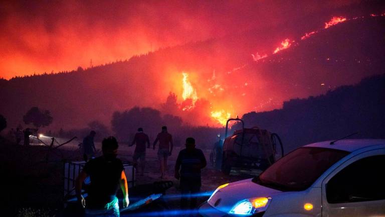 People and firefighters attempt to extinguish the flames as smoke and flares rise from a forested area following a wildfire in the Seferihisar district of Izmir, Turkey, on June 30, 2025. (Photo by Ahmet Ayberk Cimen / AFP)