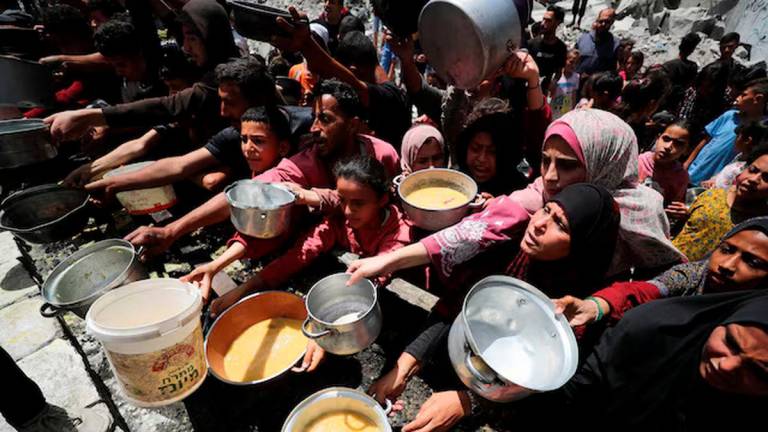 Palestinians wait to receive food cooked by a charity kitchen, in Jabalia, in the northern Gaza Strip, May 19, 2025. REUTERS/Mahmoud Issa/File Photo