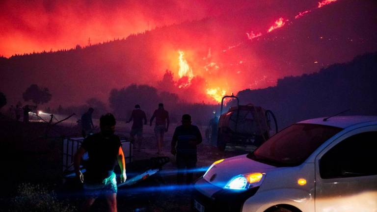 People and firefighters attempt to extinguish the flames as smoke and flares rise from a forested area following a wildfire in the Seferihisar district of Izmir, Turkey, on June 30, 2025 - AFPPIX
