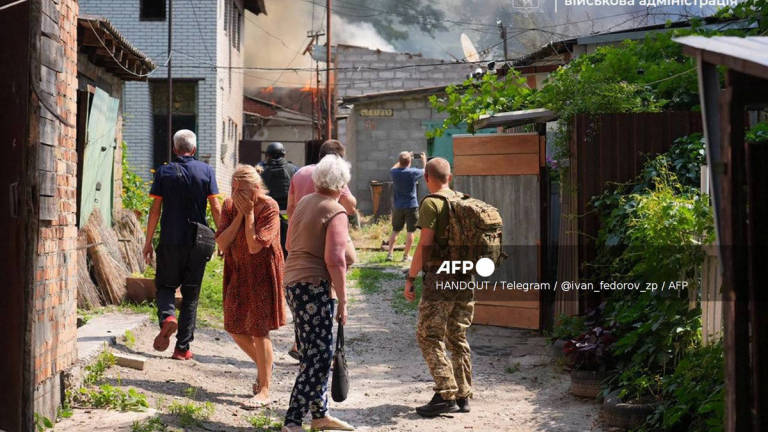This handout photograph published on July 7, 2025 on the official Telegram channel of the head of the Zaporizhzhia Regional Military Administration Ivan Fedorov, shows a woman reacting as others look at a building engulfed in flames following a Russian attack in Zaporizhzhia, amid the Russian invasion of Ukraine. - (Photo by Handout / Telegram / @ivan_fedorov_zp / AFP) / XGTY