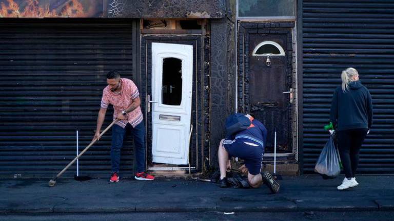 Restaurant owner Luqman Khan clears debris from the street in front of his restaurant in Middlesbrough, following rioting and looting the day before - AFPpix