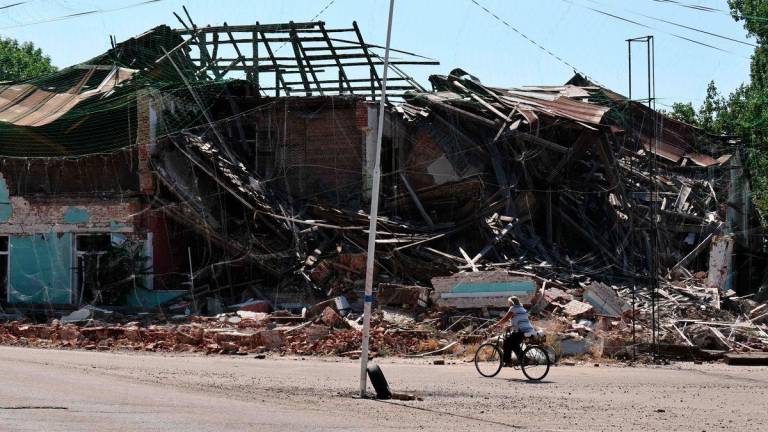 In this handout photograph taken and released by the press service of the 65th Mechanized Brigade of Ukrainian Armed Forces on July 15, 2025, a woman rides a bicycle near damaged buildings and anti-drone nets in Orikhiv, Zaporizhzhia region, amid the Russian invasion of Ukraine. - AFPPIX/65th Mechanized Brigade of Ukrainian Armed Forces