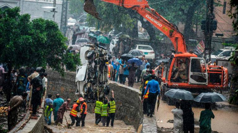 Rescuers and people look as a crane removes the wreckage of a van from a drainage after heavy monsoon rains in Islamabad on July 21, 2025. (Photo by M ASIM KHAN / AFP)