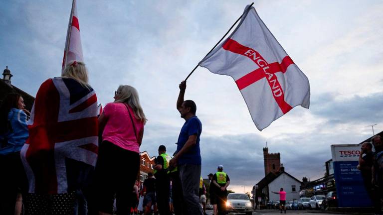 A man waves a flag with 'England' written on it, as protesters gather during an anti-immigration demonstration, following Tuesday's High Court ruling in London that granted a temporary injunction to stop asylum seekers from being housed at the The Bell Hotel, in Epping, Britain, August 24, 2025. - REUTERSPIX