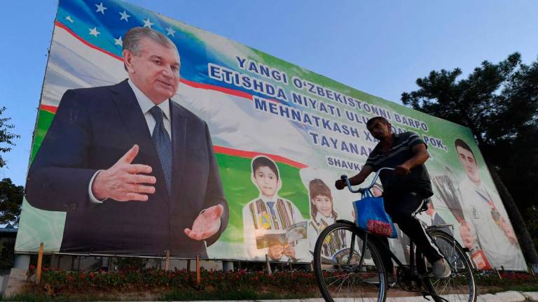 (FILES) A man rides a bicycle in front of a banner displaying Uzbek President Shavkat Mirziyoyev in the center of Termez near the Uzbek-Afghan border about 700 km from Tashkent, on August 15, 2025. Prisoners in Uzbekistan will be able to plead for reduced sentences if they read books selected by authorities to cultivate “correct spiritual and moral values”, officials said. (Photo by Vyacheslav OSELEDKO / AFP)