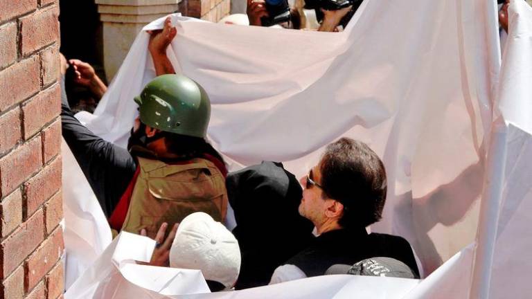 Pakistan’s former Prime Minister Imran Khan and his wife Bushra Bibi are covered with a white sheet as they arrive to appear at the High Court in Lahore - REUTERSpix