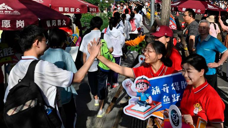 School staff members welcome students as they enter a school during China’s National College Entrance Examination (NCEE), known as “gaokao” - AFPPIX