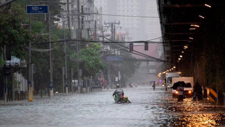 A cyclist crosses a flooded street in Manila on July 22, 2025, after heavy rains caused floodings enhanced by monsoon. (Photo by Ted ALJIBE / AFP)