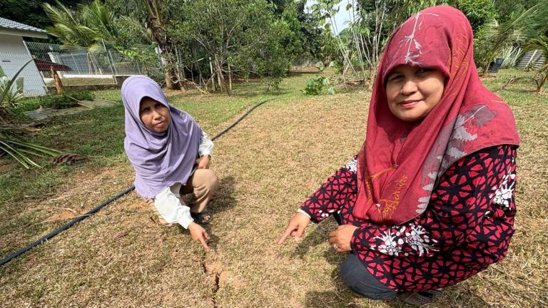 Penduduk Jalan Buloh Kasap, Batu 2 Ramlah Ishak, 56, (kiri) bersama kakaknya Umi Kalsom Ishak, 58, menunjukkan kesan rekahan tanah ketara di kawasan kebun di bahagian belakang rumah yang dipercayai berpunca daripada gegaran gempa bumi ketika ditemui Bernama, di sini hari ini- fotoBERNAMA