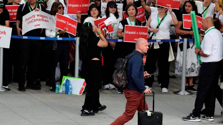 FILE PHOTO: A passenger walks as striking Air Canada flight attendants hold placards as they defy a back to work order at Vancouver International Airport in Richmond, British Columbia, Canada August 18, 2025. REUTERS/Chris Helgren/File Photo/File Photo