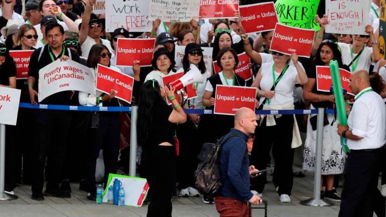 FILE PHOTO: A passenger walks as striking Air Canada flight attendants hold placards as they defy a back to work order at Vancouver International Airport in Richmond, British Columbia, Canada August 18, 2025. REUTERS/Chris Helgren/File Photo/File Photo