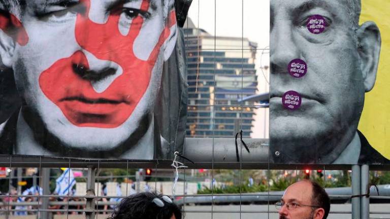 A man and woman sit under images of Israeli Benjamin Netanyahu during an anti-government rally in Tel Aviv - AFPpix