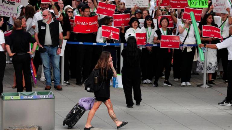 A passenger walks as striking Air Canada flight attendants hold placards as they defy a back to work order at Vancouver International Airport in Richmond, British Columbia, Canada August 18, 2025. - REUTERSPIX