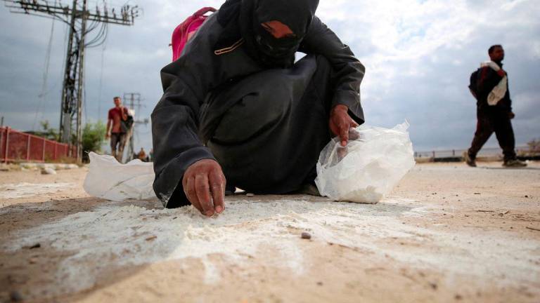 A woman collects flour from the ground as Palestinians receive aid supplies from the U.S.-backed Gaza Humanitarian Foundation (GHF), in the central Gaza Strip, August 1, 2025. - REUTERSPIX