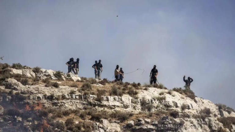 Masked Israeli settlers hurl rocks at Palestinians from hilltop in the West Bank village of Sinjil on July 4, 2025. - AFP
