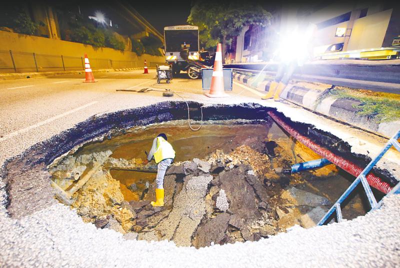 A workman inspecting pipes that were exposed after a huge sinkhole caused part of Jalan Loke Yew in Kuala Lumpur to cave in on Sunday. — BBXpress