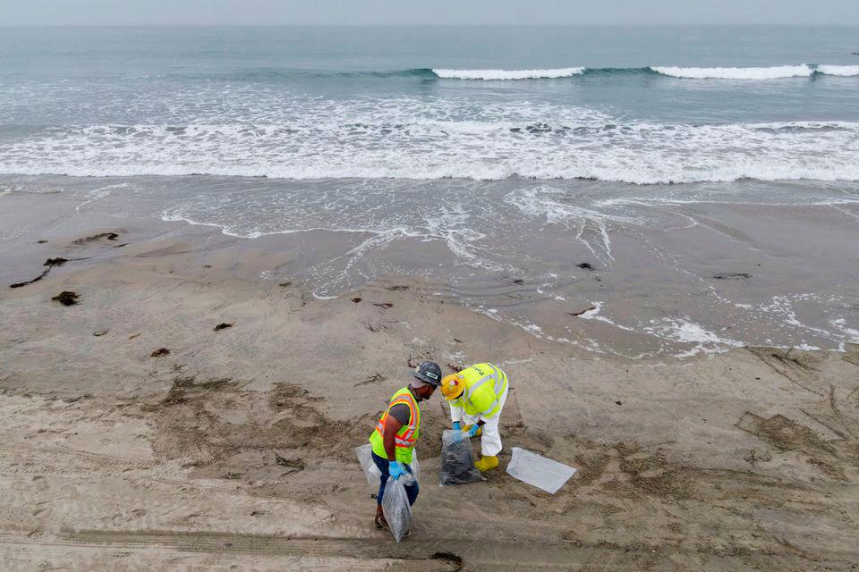Workers rake up crude oil, after more than 3,000 barrels (126,000 gallons) of crude oil leaked from a ruptured pipeline into the Pacific Ocean in Newport Beach, California, U.S., October 7, 2021. Picture taken with a drone. - REUTERSPIX