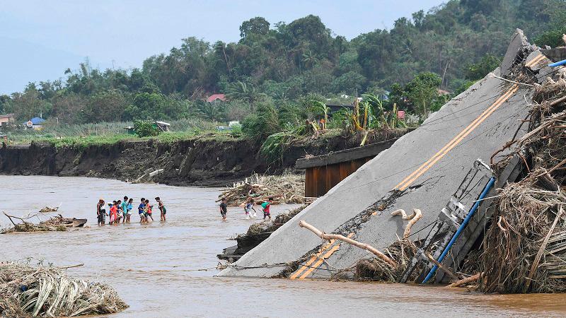 People cross a river next to a bridge that collapsed after the river overflew due to heavy rains brought about by Tropical Storm Trami in Laurel, Batangas province, south of Manila on October 25, 2024. Philippine rescue workers battled floodwaters on October 25 to reach residents still trapped on the roofs of their homes as Tropical Storm Trami moved out to sea after killing at least 40 people. - Ted ALJIBE / AFP