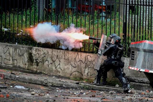 A riot police officer fires tear gas at demonstrators in Colombia, where anti-government protests have turned deadly. — AFP