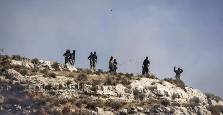 Masked Israeli settlers hurl rocks at Palestinians from hilltop in the West Bank village of Sinjil on July 4, 2025. - AFP