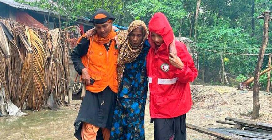 A Bangladesh Red Crescent volunteer helps a lady away from her flooded home following Cyclone Remal. The response was part funded through an IFRC-DREF allocation. - Photo: BRCS