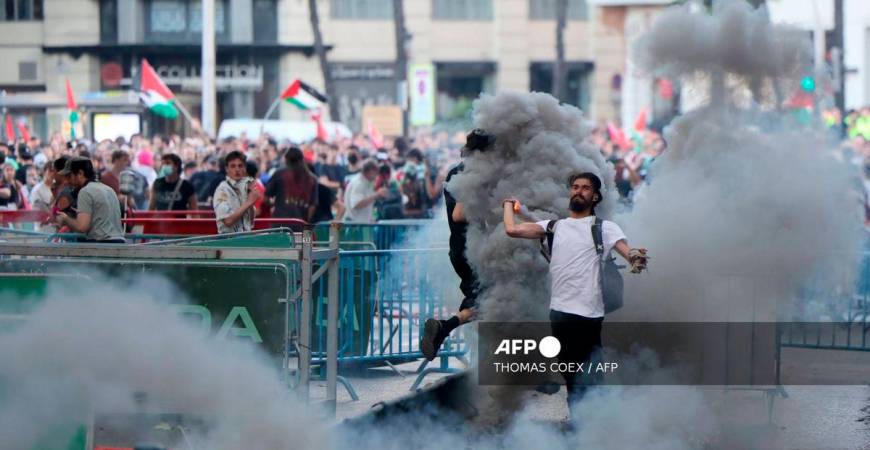 A man throws back to police a tear gas canister after Pro-Palestinians protestors invaded the street during the 21st and last stage of the Vuelta a Espana 2025, in Madrid on September 14, 2025. - AFP