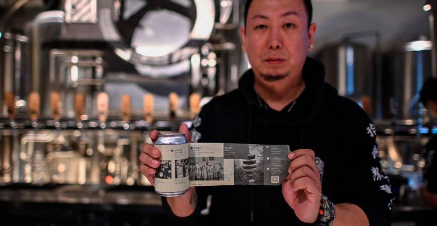 This photo taken on November 20, 2020 shows Wang Fan, founder of the No. 18 Brewery, posing with one of his beers with images of the city’s fight against the Covid-19 coronavirus in Wuhan, China’s central Hubei province. AFP / Hector RETAMAL