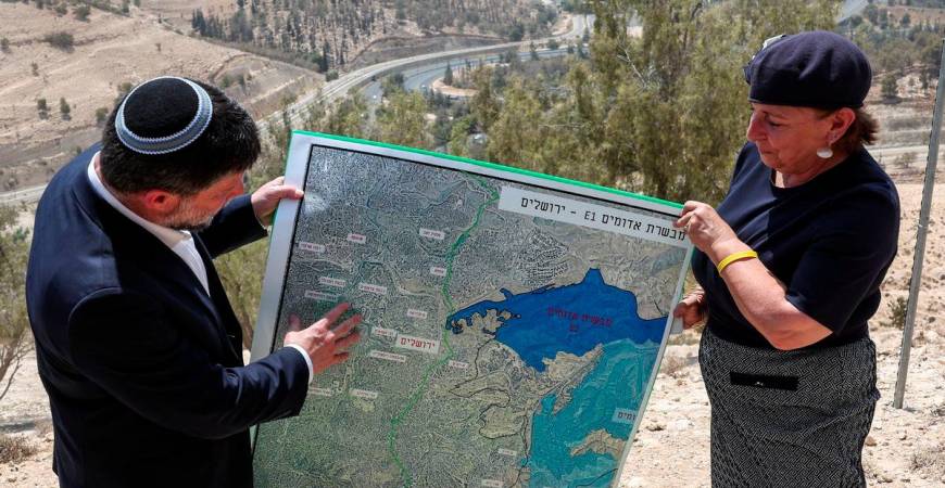 Israeli Finance Minister Bezalel Smotrich and a woman hold a map that shows the long-frozen E1 settlement scheme, that would split East Jerusalem from the occupied West Bank, on the day of a press conference near the Israeli settlement of Maale Adumim, in the Israeli-occupied West Bank, August 14, 2025. - REUTERSPIX