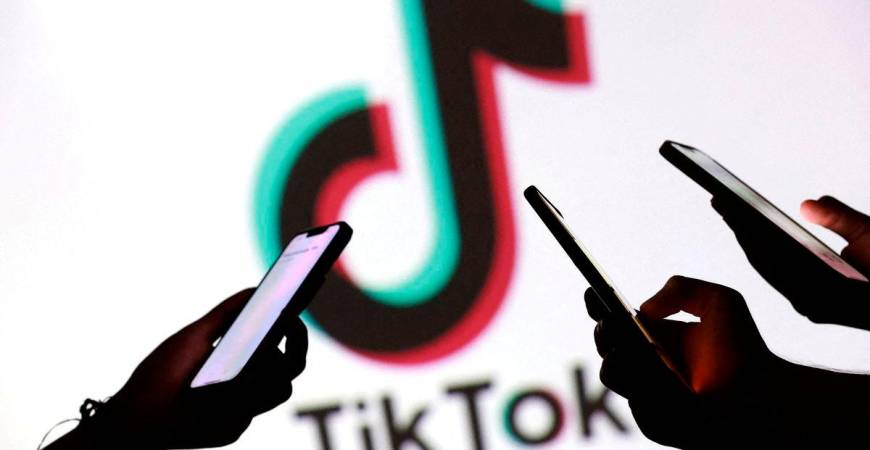 FILE PHOTO: Teenagers pose for a photo while holding smartphones in front of a TikTok logo in this illustration taken September 11, 2025. REUTERS/Dado Ruvic/Illustration/File Photo