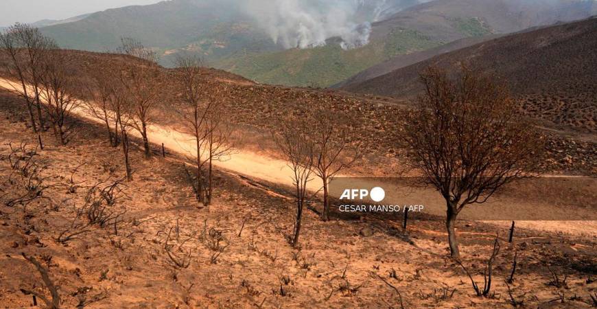 This picture taken from a burned area at the Orellana viewpoint in the Roman-era mining site of Las Medulas in the municipality of Carucedo, shows a wildfire in the background, on August 11, 2025. - Cesar Manso / AFP