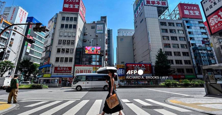 A woman (C) carries an umbrella to shelter from the sun as pedestrians cross a street in the Kabukicho entertainment area of Shinjuku in central Tokyo on July 29, 2025. - Richard A. Brooks / AFP
