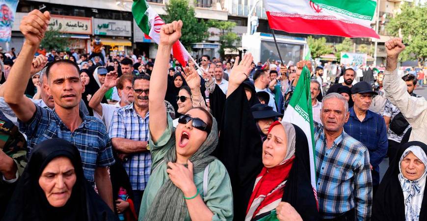 Iranians lift flags and chant during a rally protesting the US attack on Iran in Enghelab Square in Tehran on June 22, 2025. Iran’s President Masoud Pezeshkian condemned US strikes on nuclear sites on June 22, saying in his first response that the attack revealed Washington was “behind” Israel’s military campaign in the Islamic republic. - ATTA KENARE / AFP