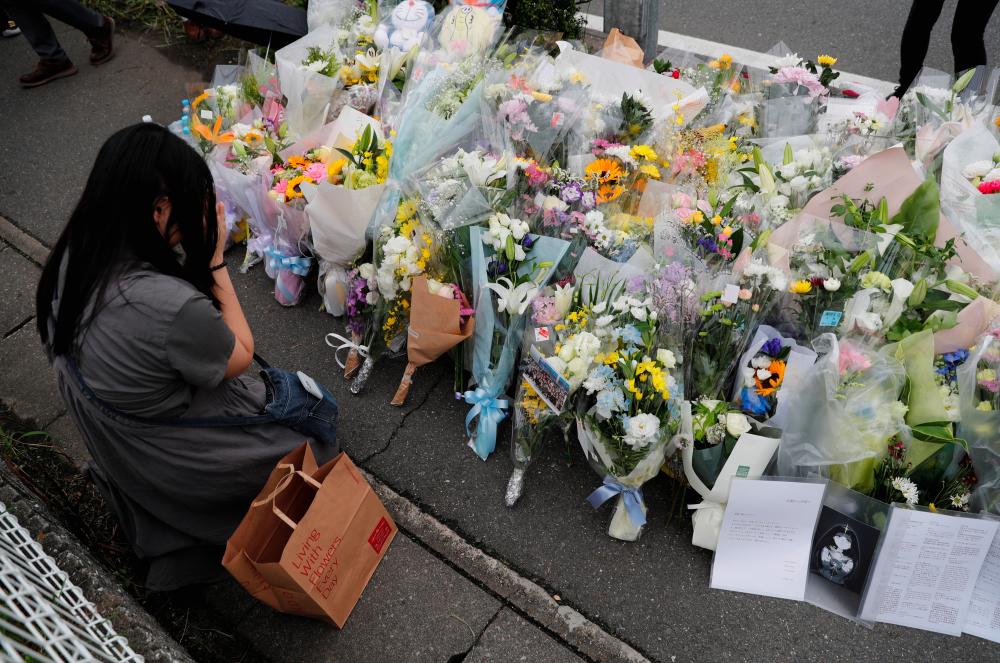 A woman prays in front of a row of flowers placed for victims of the torched Kyoto Animation building in Kyoto, Japan, July 20, 2019. - Reuters