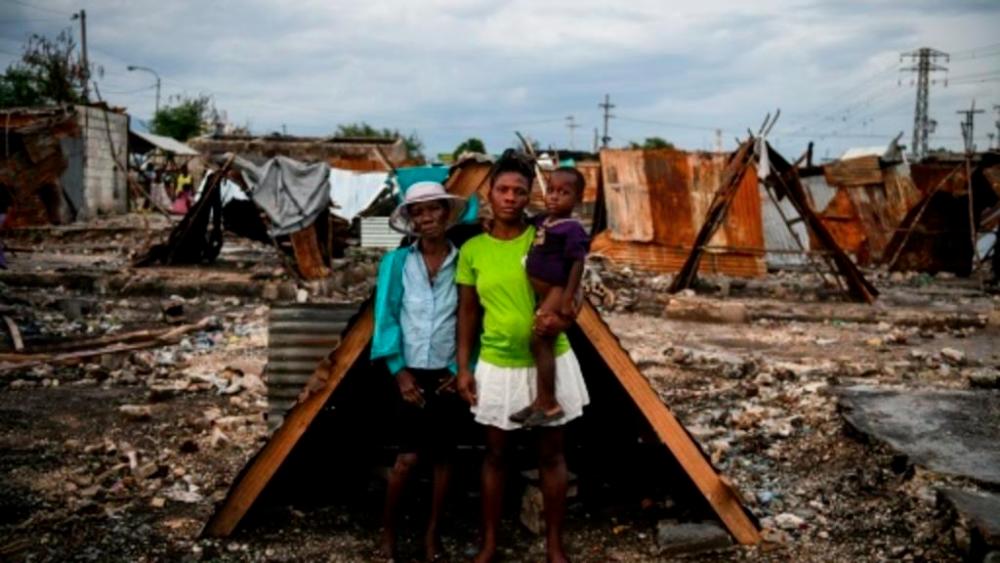 Iris Daniel, 57, Lovely Saint-Pierre, 32, and Evanston Daniel, 5, pose on May 25, 2019, outside a makeshift shelter on the site of their home which was burned during a November 2018 gang war in Port-au-Prince. — AFP