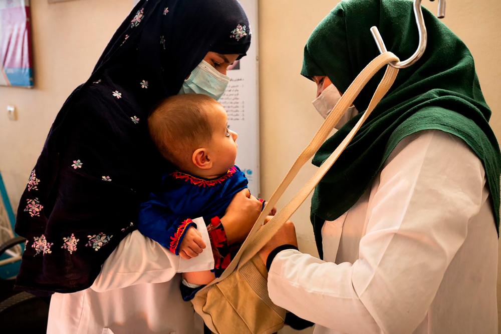 This picture taken on October 6, 2021 shows a midwife (L) and a nutrition counsellor weighing a baby at the Tangi Saidan clinic run by the Swedish Committee for Afghanistan, in Daymirdad district of Wardak province.AFPpix