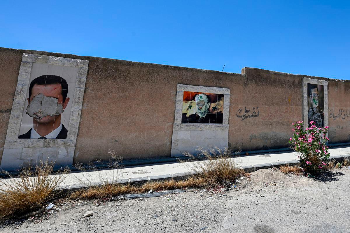 Defaced portraits of Syria’s ousted president Bashar al-Assad (L) and his late father Hafez al-Assad (C) hang on a wall in the capital Damascus on June 2, 2025. (Photo by LOUAI BESHARA / AFP)