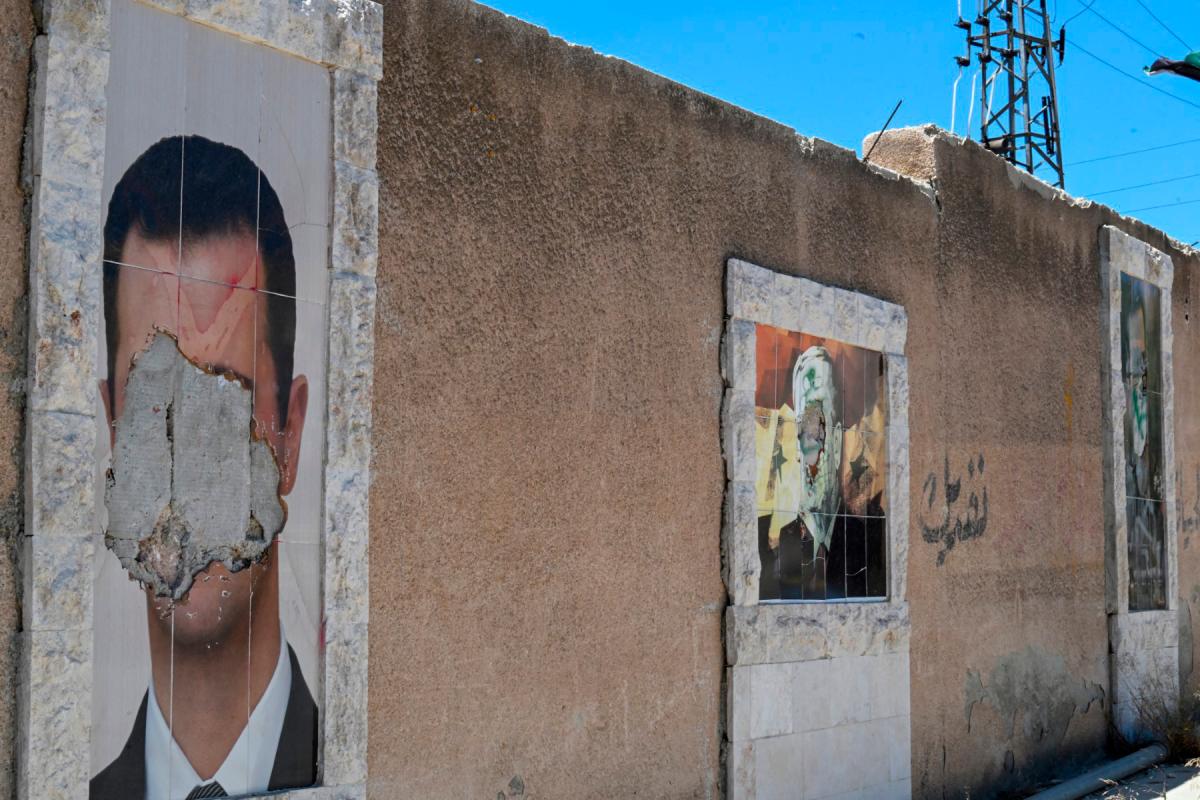 Defaced portraits of Syria’s ousted president Bashar al-Assad (L) and his late father Hafez al-Assad (C) hang on a wall in the capital Damascus on June 2, 2025. (Photo by LOUAI BESHARA / AFP)