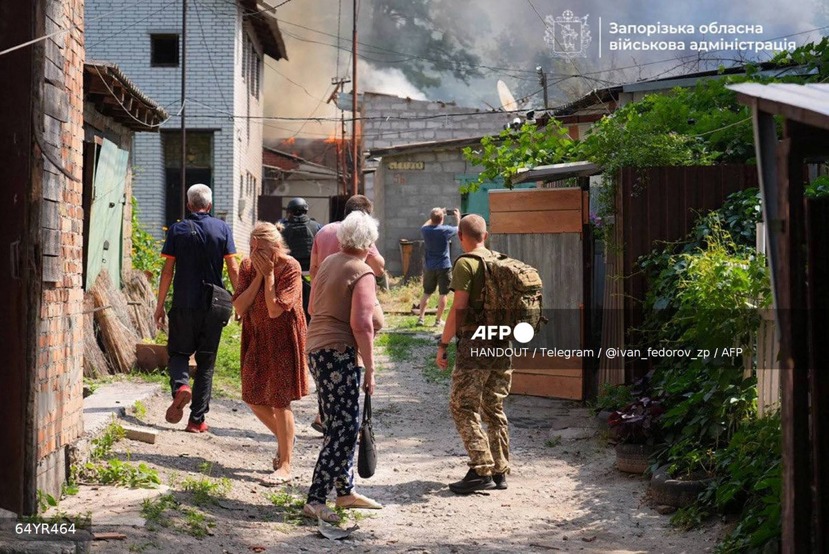 This handout photograph published on July 7, 2025 on the official Telegram channel of the head of the Zaporizhzhia Regional Military Administration Ivan Fedorov, shows a woman reacting as others look at a building engulfed in flames following a Russian attack in Zaporizhzhia, amid the Russian invasion of Ukraine. - (Photo by Handout / Telegram / @ivan_fedorov_zp / AFP) / XGTY