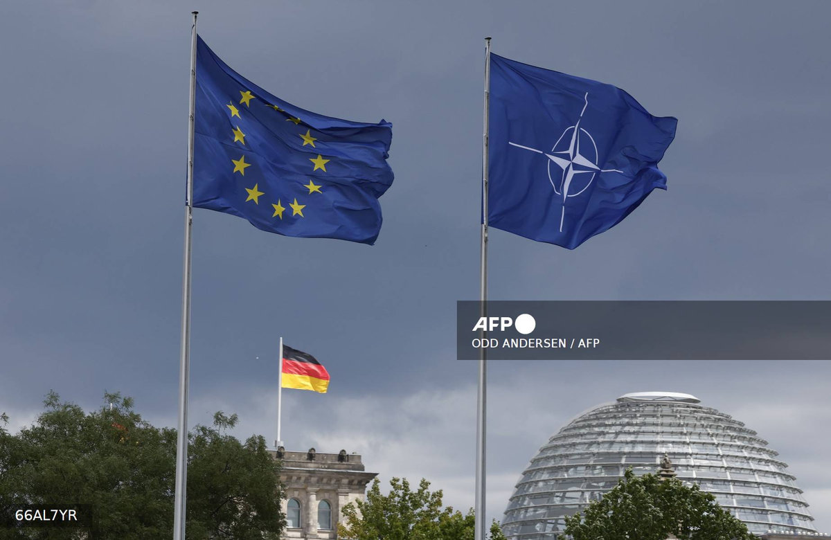 The EU, German and NATO flag fly backdropped by the Reichstag building that houses the Bundestag (lower house of Parliament) ahead a ceremony to mark Germany's 70 years in NATO in Berlin, on July 9, 2025. - AFP